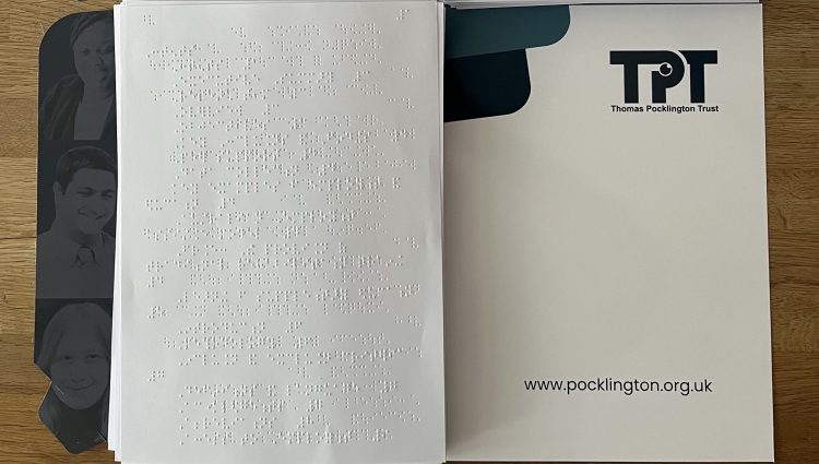 photo shows two braille versions of the international report, placed on a table displaying TPT logos, contact details and social media presence