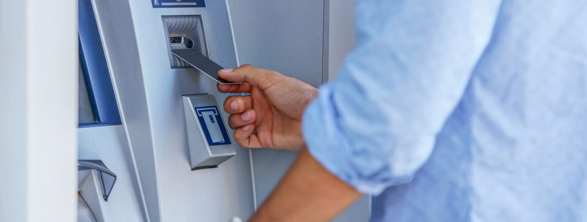 Image shows a man putting his card into an ATM