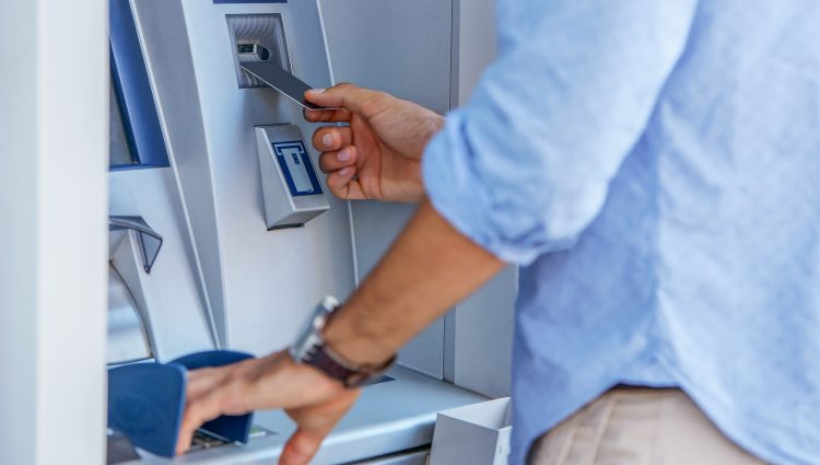 Image shows a man putting his card into an ATM