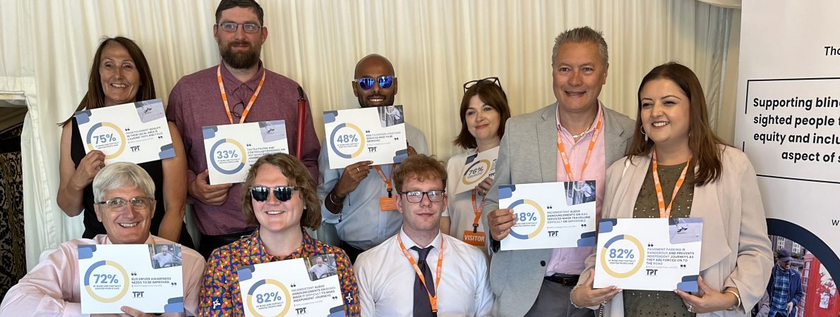 9 TPT staff and volunteers hold up placards showing survey statistics of issues impacting blind and partially sighted people.