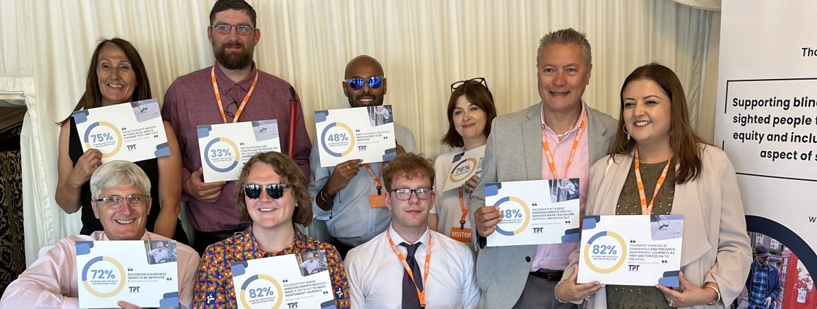 9 TPT staff and volunteers hold up placards showing survey statistics of issues impacting blind and partially sighted people.