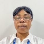 Annie is standing against a light coloured wall, wearing a white shirt and a blue lanyard which reads "Student" and "ARTS UNIVERSITY".