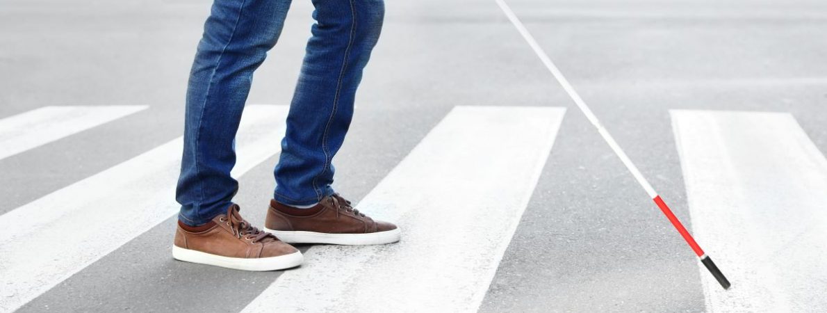 A blind person holding a cane crossing the road