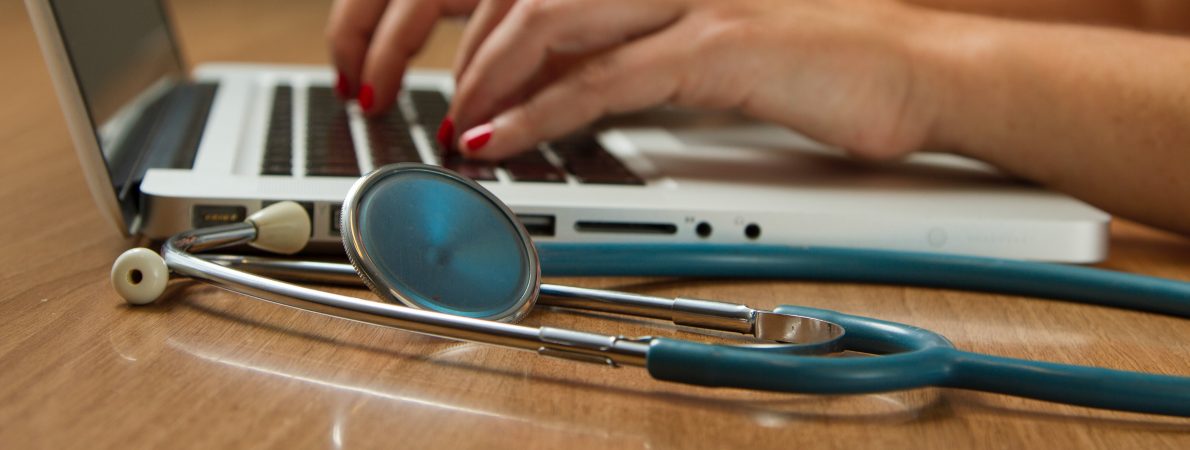 Doctor typing on a laptop with a stethoscope in the foreground