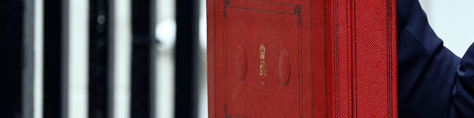 A close up of the Chancellor's Red Box held up by a hand with painted red nails.