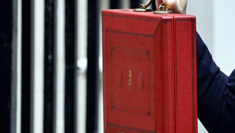 A close up of the Chancellor's Red Box held up by a hand with painted red nails.