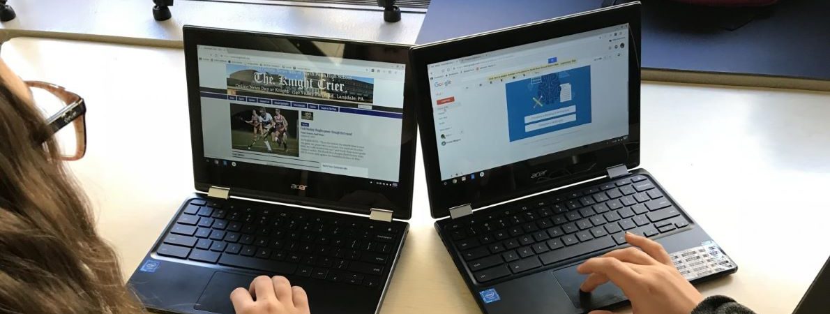 A picture of two students sitting at a table, typing on Chromebook laptops.