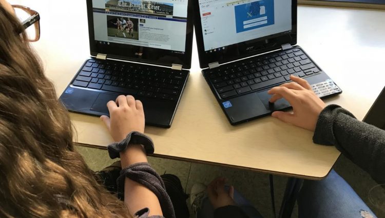 A picture of two students sitting at a table, typing on Chromebook laptops. | links to article: Google ChromeBook: Built-in Accessibility Features