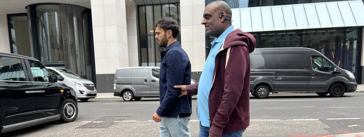Sighted guide guiding an SLC volunteer with a guide dog , cross the road.