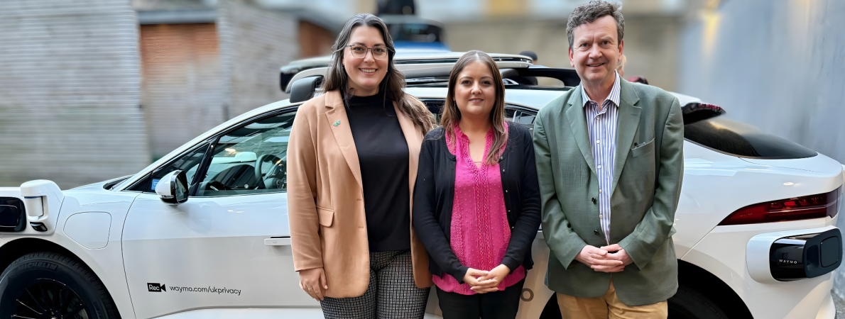 Amanda from Waymo, Bhavini, our Policy and Campaigns Manager and Charles, our CEO stand side by side in front of a white, electric Waymo car.