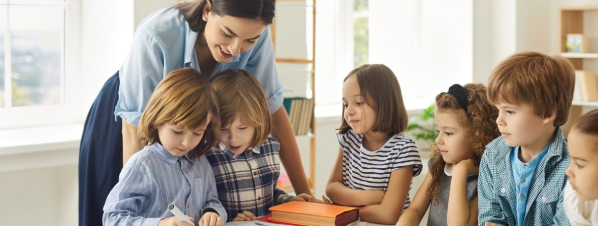 Young school teacher helping her students who are writing in notebooks.