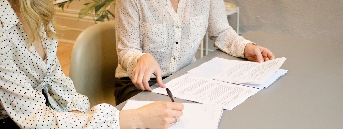 Two women sit at a desk filling in a form
