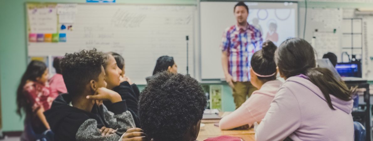 Children sitting at desks in a classroom with their backs to the camera