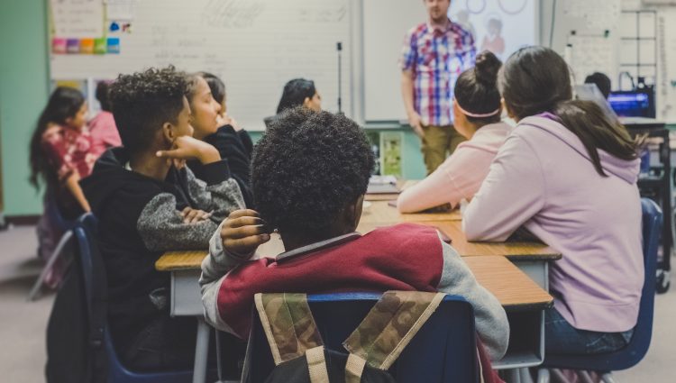 Children sitting at desks in a classroom with their backs to the camera | links to article: What is an Education Health and Care Plan?