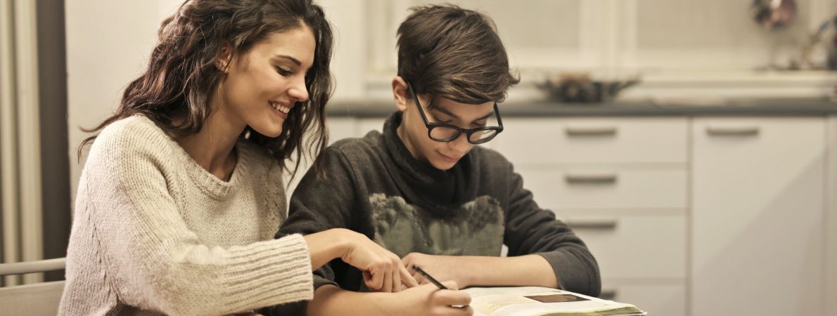 A woman and boy sit at a kitchen table doing homework