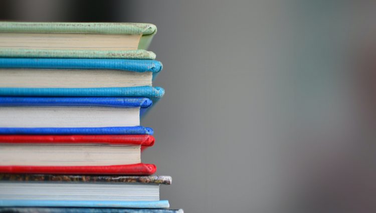 A stack of multicoloured books with a grey background | links to article: Support in Education Guides