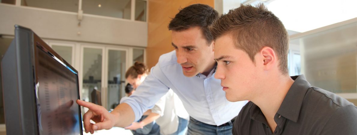 A man showing a younger man something on a computer's screen