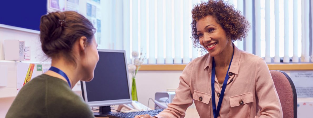 Two women sit at a desk smiling