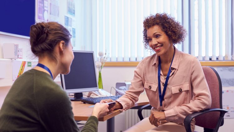 Two women sit at a desk smiling | links to article: What is an EHCP Annual Review?