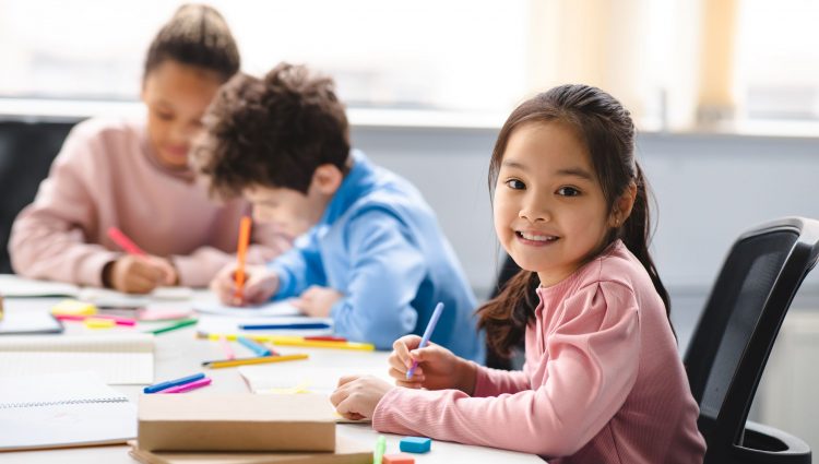 A young girl smiling at the camera in a classroom | links to article: How Do I Apply For an EHCP?