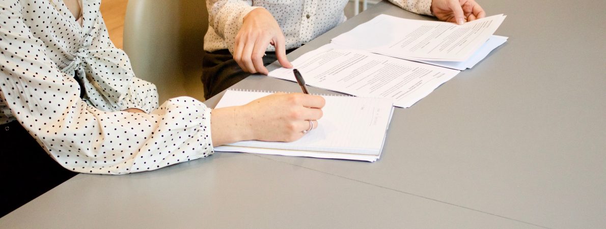 Two women sit at a desk filling in a form