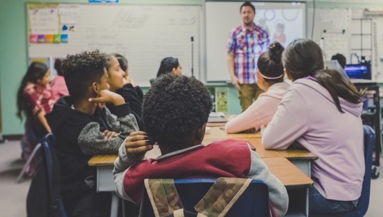 Children sitting at desks in a classroom with their backs to the camera | links to article: What Support is Available at Secondary School?