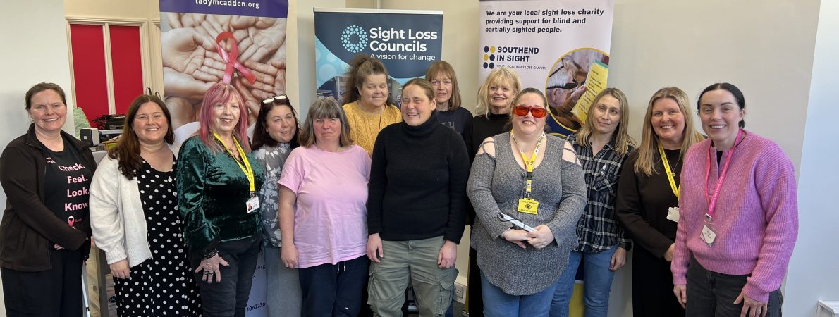 Blind and partially sighted attendees at Essex SLC's breast cancer screening awareness event are stood alongside Amy Askew, Engagement Manager for Thomas Pocklington Trust, Angela and Lauren from Lady McAdden, and Lucy from Southend in Sight. They are stood facing the camera, smiling.