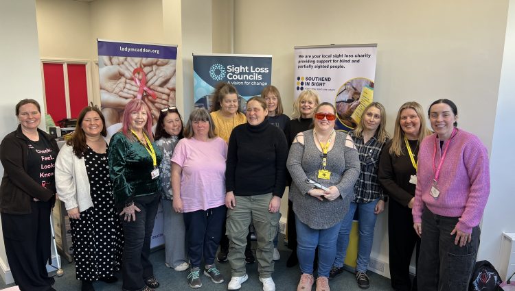 Blind and partially sighted attendees at Essex SLC's breast cancer screening awareness event are stood alongside Amy Askew, Engagement Manager for Thomas Pocklington Trust, Angela and Lauren from Lady McAdden, and Lucy from Southend in Sight. They are stood facing the camera, smiling.