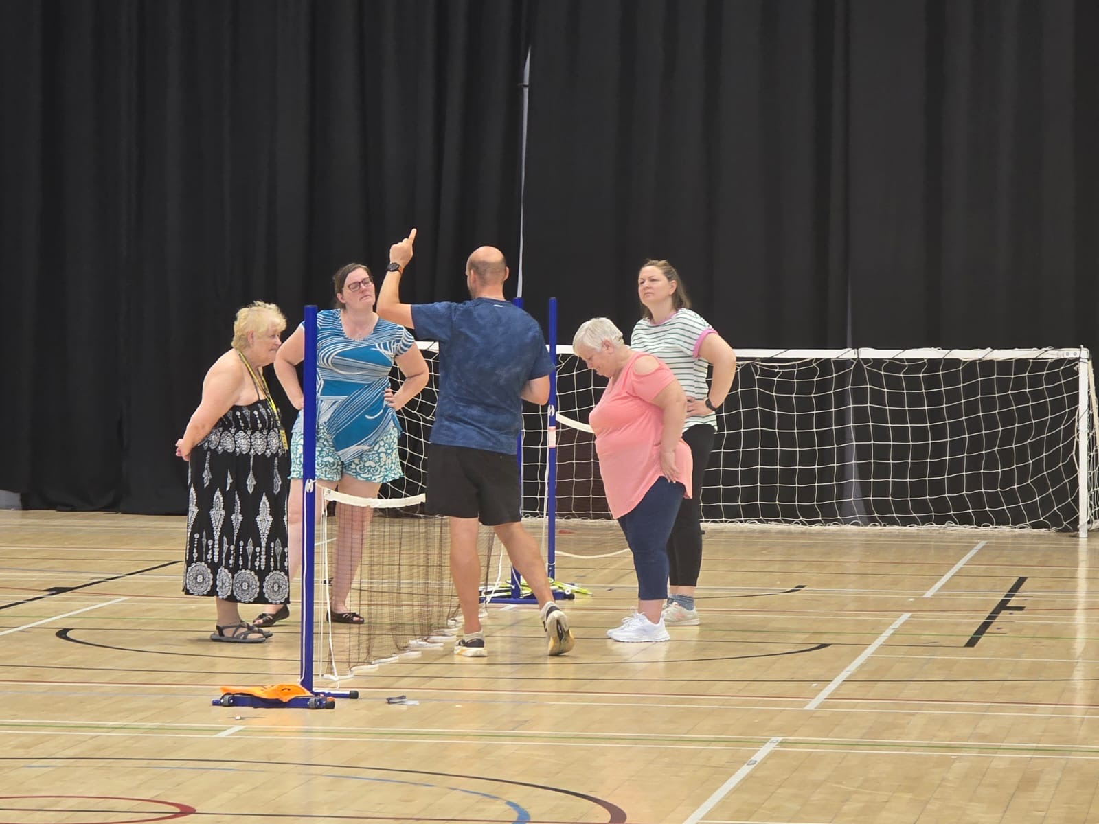 Four females listening to a coach at a tennis net in a sports hall, during South Yorkshire SLC's Let's Get Active Event.
