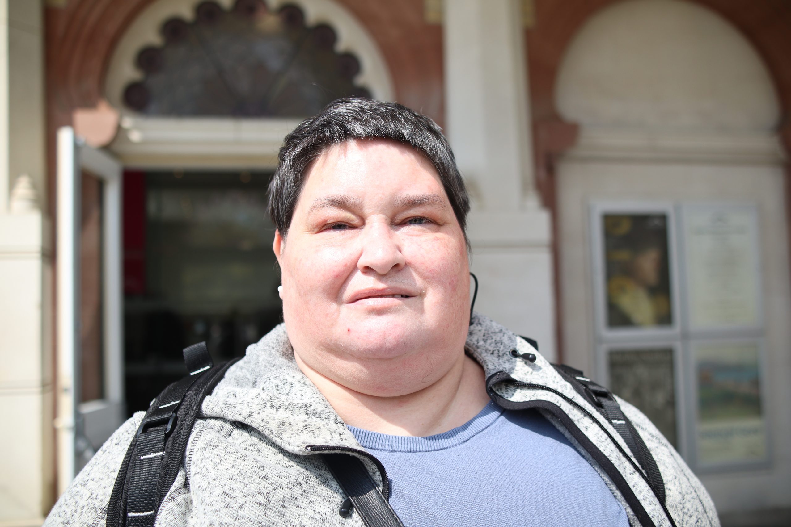 Headshot of Iris Keppler, Sussex SLC member. Iris is wearing a white t-shirt and beige coat and is smiling at the camera.