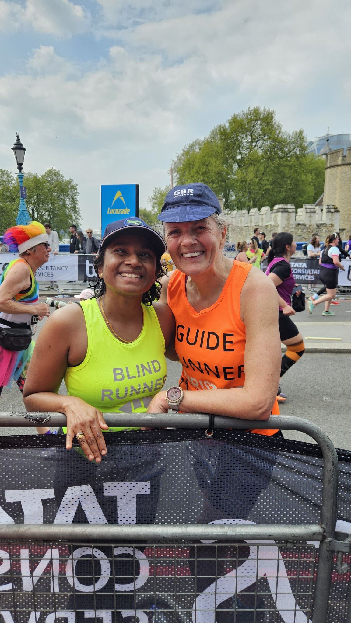 Deepika and guide runner leaning over barrier for a photo at the marathon. They are smiling.