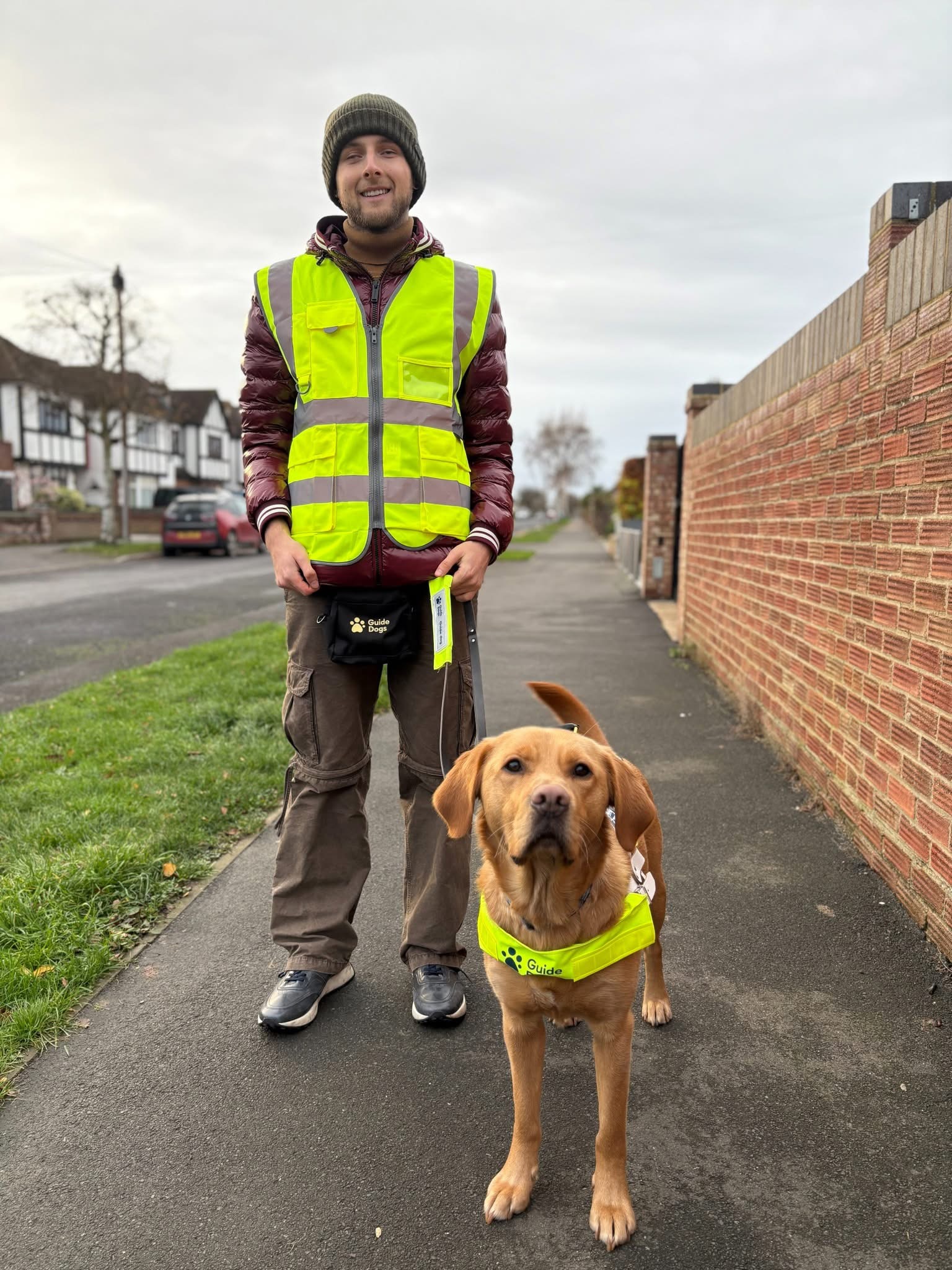 A man standing with his guide dog on a footpath next to a street