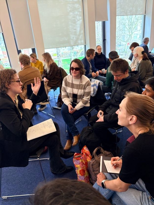 Image of mixed group of people discussing a topic sat in a semi circle in chairs. 