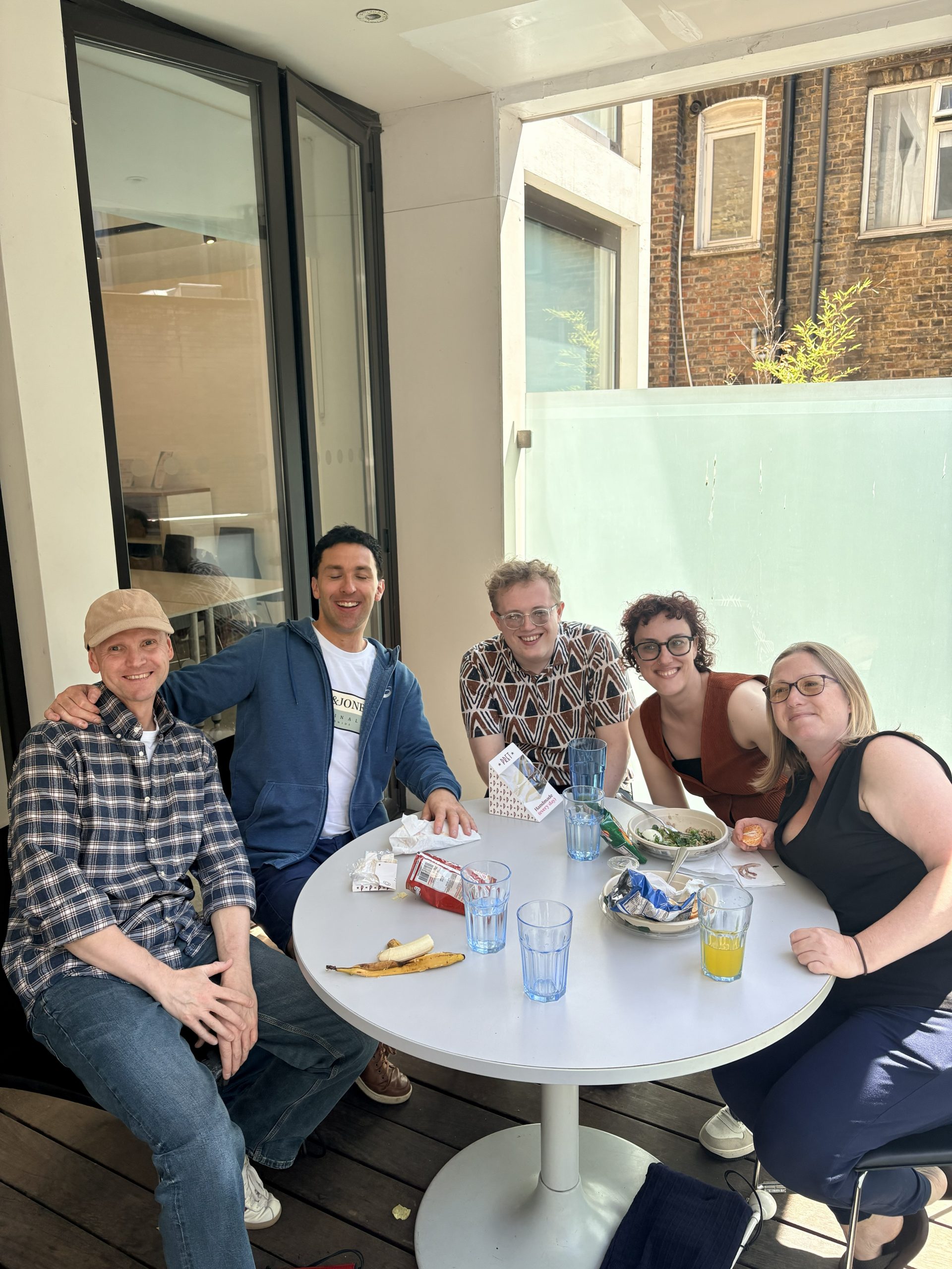 Several people smile for a photo at a table eating food.