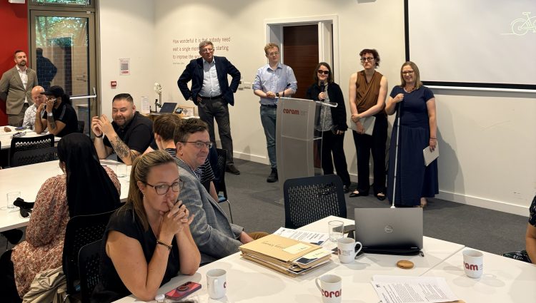Several people presenting at the front of a conference room while attendees sit at tables and listen during a workshop or meeting. | links to article: Get Set Progress: A Celebration of Achievement