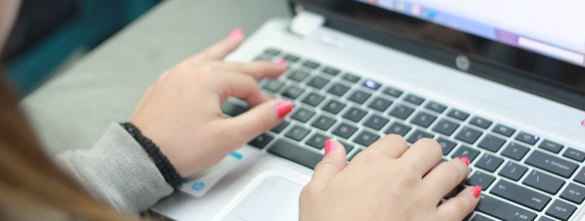 A picture of hands typing on a black laptop keyboard.