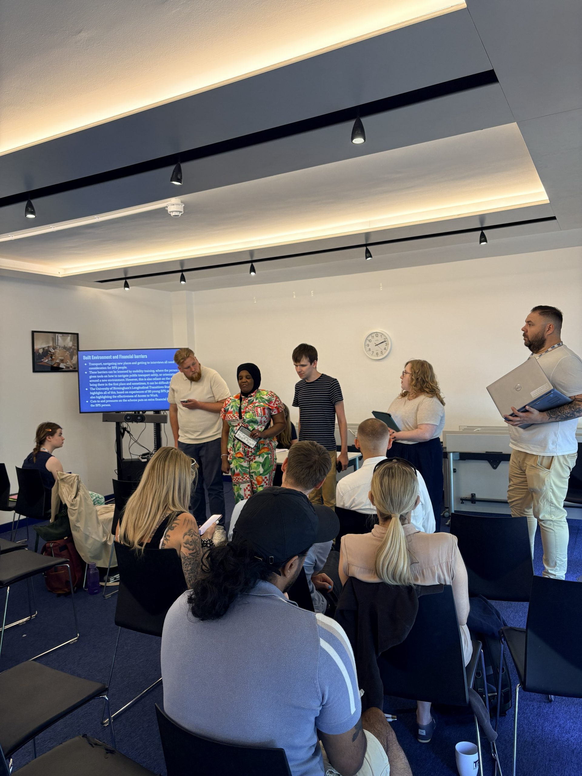 Several people present to a group of people sitting in front of them in a large room.